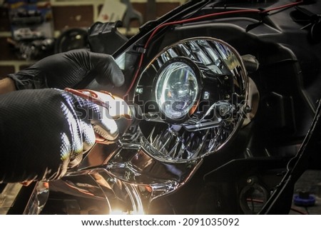 Car headlight in repair close-up. An auto mechanic wearing gloves installs the lens into the headlight housing. The concept of a car service.Installation of LED lenses in the headlight. LED lenses. Royalty-Free Stock Photo #2091035092