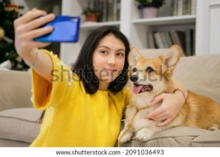 Teenage girl taking selfie with her dog at home. Dog lover with domestic animal. Modern technology, people and animals concept.