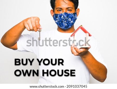 A high key picture of men holding key and house miniature with buy your own house word. Property ownership, mortgage and tenancy concept.