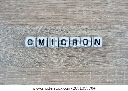 A white cube written Omicron over wooden table. New Variant. Coronavirus Mutation
