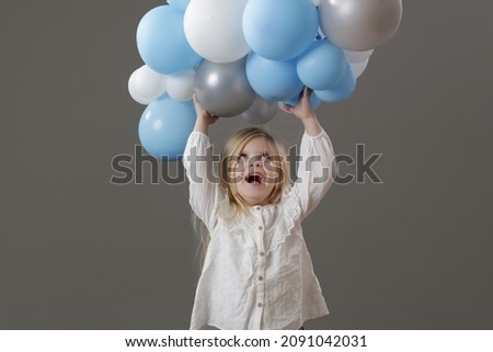 Studio portrait of happy little girl holding a group of white and blue balloons. Concept of celebration, happiness, wishes and hopes.	