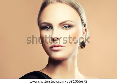 Close-up headshot portrait of model woman looking at camera. Make-up, perfect skin, jewelry. Beige background