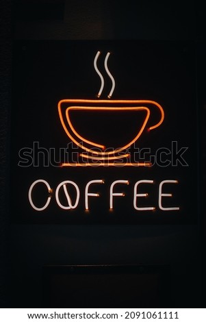 Bright orange neon sign with a picture of a coffee cup and text coffee on a dark background