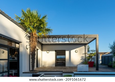 Trendy outdoor patio pergola surrounded by landscaping. shade structure with awning and patio roof and aluminium grill.  Royalty-Free Stock Photo #2091061672