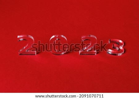 Photo of numbers 2023 made of thick clear acrylic glass on a red background. Selective focusing.