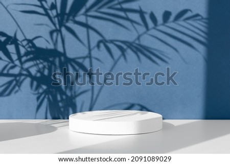 Minimal abstract blue and white background for eco cosmetic product presentation. Cylindrical white scene. Premium podium with a shadow of tropical palm leaves. Empty showcase.
