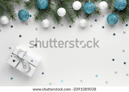 Christmas border of shiny white and blue balls, evergreen branches of a xmas tree and a gift on a white background with sequins. New Year's card.
