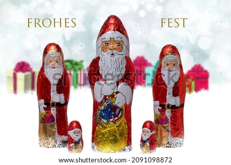 Christmas greeting card. Closeup of various cheerful wrapped chocolate Santa Claus over festive abstract blurred gift boxes. Merry christmas text in german. Macro.