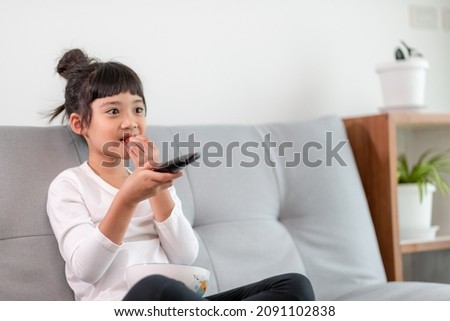Kid with remote control sitting on the couch watching a movie on tv