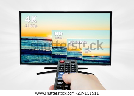 4K television display with comparison of resolutions. Remote control in hand Royalty-Free Stock Photo #209111611