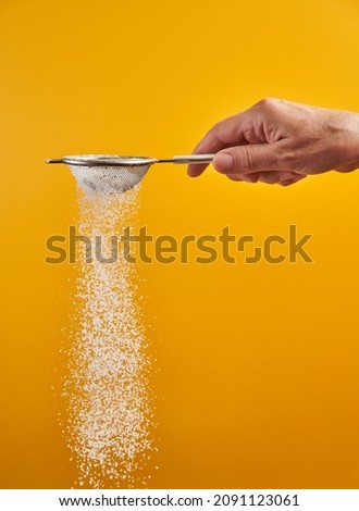 Woman's hand sprinkling powdered sugar with a sifter, isolated on yellow background