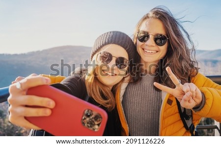 Two happy cheerful young girls in sunglasses traveling together taking selfie on smartphone