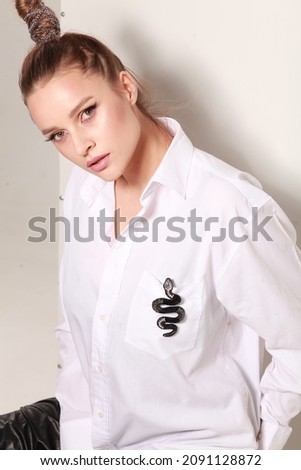 Young model with make up wearing white shirt with attached snake decor pin broach. Luxury handmade jewellery for glamour lifestyle. Hobby accessory for present. Studio shot over white background