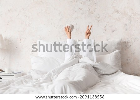 Young woman with cup showing PEACE in bedroom