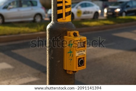 Crosswalk button for pedestrian with light warning. Defocused background with Cars drive along road and bokeh from headlights. The inscription in Czech -Tlačítko pro chodce- Button for pedestrians.  
