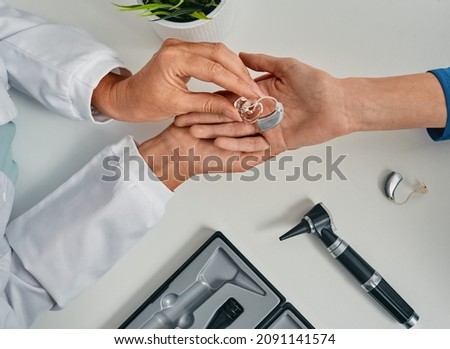 Audiologist puts modern BTE hearing aid in patient hand for treatment deafness at hearing clinic, top view. Hearing solutions Royalty-Free Stock Photo #2091141574