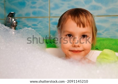 A cute baby in the bath is washing with soap foam.