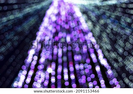 Festive purple xmas lights on christmas tree in urban central park at holiday winter night, defocus shiny garland decoration glow in lilac bokeh in dark downtown, out of focus image