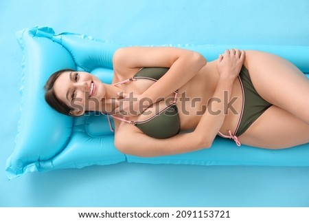 Beautiful young woman lying on inflatable mattress against color background