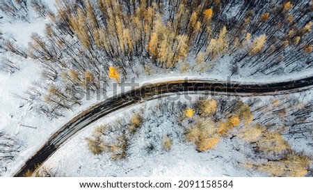 Aerial high angle view of narrow winding curvy mountain road among the trees in winter forest. Snowy landscape, bird's eye view. Royalty-Free Stock Photo #2091158584