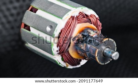 Damaged scorched commutator due to short circuit in rotor winding of DC electric motor. Detail of charred electromotor part with copper wire and metal laminations on blurred black netting background. Royalty-Free Stock Photo #2091177649