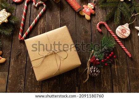 Christmas gift wrapped in eco paper placed on a wooden table with holiday decoration, candy canes and Christmas cookies, happy holidays concept