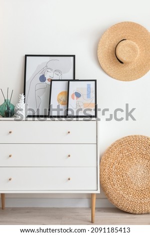Chest of drawers with pictures and decor near light wall