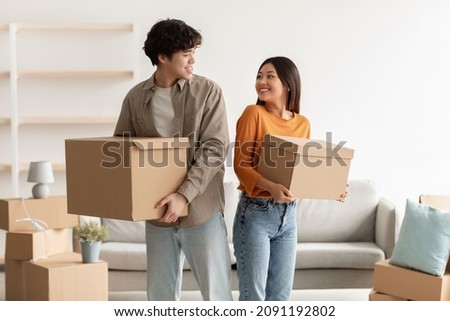 Home relocation concept. Positive young Asian couple carrying carton boxes in their owned house. Portrait of millennial tenants with belongings moving into new property Royalty-Free Stock Photo #2091192802