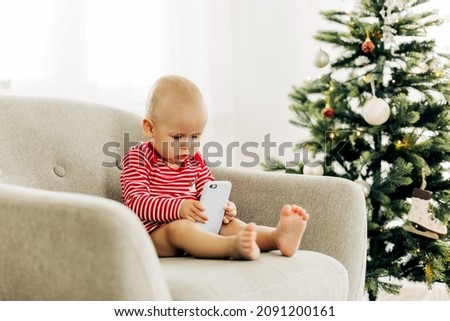 Happy boy kid watching cartoons on a smartphone in a chair next to a Christmas tree