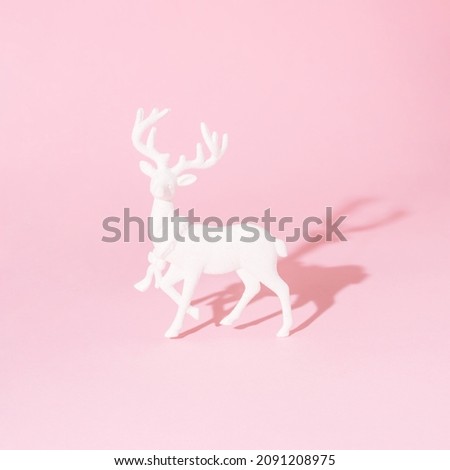 A white reindeer on pastel pink background. Minimal winter festive season creative concept for web banner or card. Surreal traditional Christmas or New Year symbolic design.