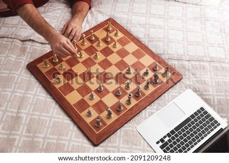 Man playing chess with partner through online video chat on bed, closeup