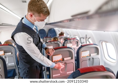 Flight attendant in face mask preparing passenger seat in airplane Royalty-Free Stock Photo #2091210340