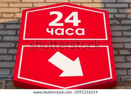 Red signboard with an arrow on a brick wall. Inscription in Russian 24 hours.