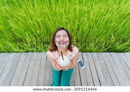 Thai girls sit and take pictures on the path in the rice fields. There is beautiful green rice. He looked up at the sky with a good smile.