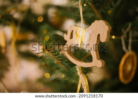 A wooden toy horse is hanging on a green branch of a fir tree. Holiday decorations. Handmade toys. Christmas and New Year.