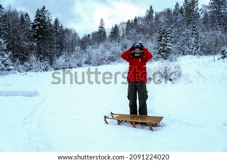 Young woman with sled. Caucasian woman in winter forest. Girl enjoys the snow falls. Close up portrait of snowboarder woman at ski resort wearing goggles with reflection of forest in mountains. 