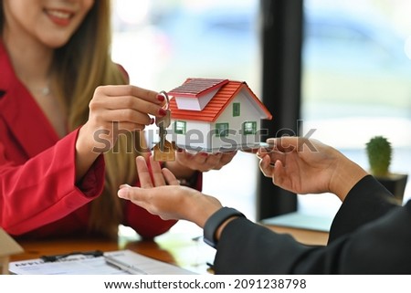 Photo of a young broker woman showing a house model while sitting together with her customer at the wooden working desk.