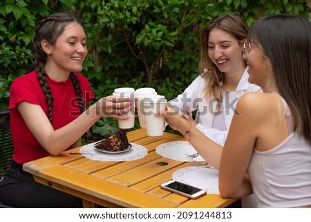 Three friends toasting with coffee and laughing. A portion of cake on the table and a cell phone