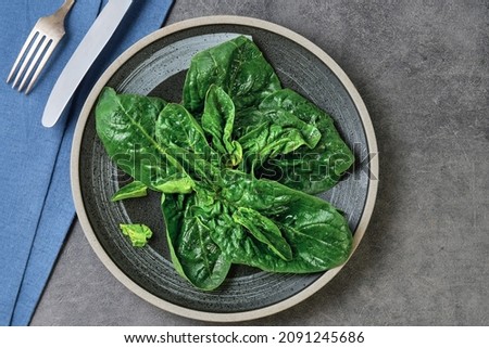 Idea of spinach leaf salad on a plate, top view. Nearby are cutlery. Spinach is an organic healthy vegetable rich in fiber and vitamins.