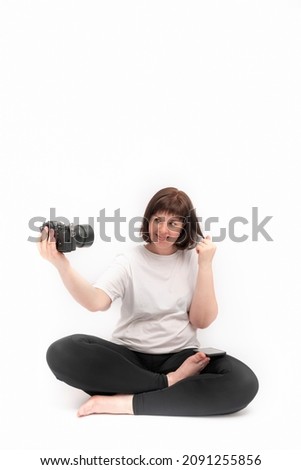 Young cheerful woman practices yoga and takes pictures of herself with camera. Portrait of girl in half lotus pose on white background