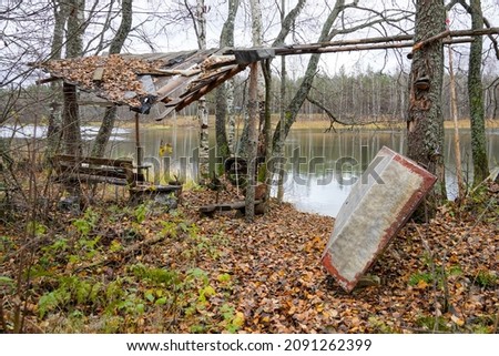 abandoned house in the woods camp of fishermen hunters on the shore of the lake in the autumn forest. broken roof and wooden bench. Homemade boat . High quality photo
