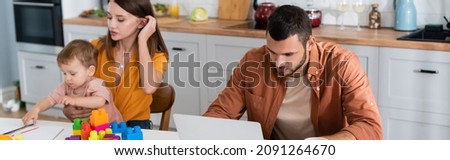 Freelancer using laptop near family playing and building blocks at home, banner