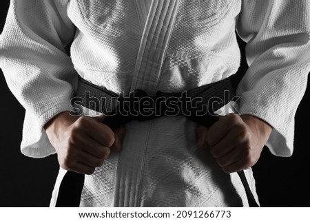 Man in keikogi tying black belt on dark background, closeup. Martial arts uniform Royalty-Free Stock Photo #2091266773