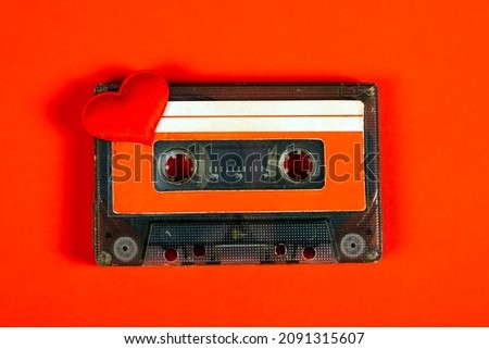 Old Audio Cassette with a Red Heart on the Red Paper Background closeup