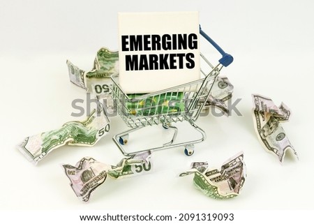 Business and economy concept. Crumpled dollars lie on a white surface, there is a cart inside a sign with the inscription - EMERGING MARKETS