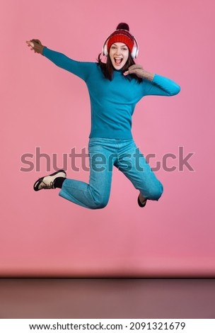 Joy, fun. Dynamic portrait of excited young girl in warm winter blue sport attire jumping isolated on pink studio background. Concept of human emotions, facial expression, youth. Copy space for ad.