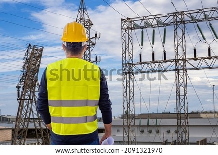 Worker in hard hat and yellow vest against the background of a power plant as an industrial energy concept