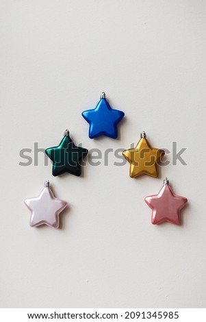 Christmas tree made of different vibrant colours star shaped ornament. Minimal New year concept on a white wall background. Holiday card or pattern. Christmas spirit.