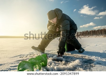 Fisherman is fishing in a hole on a large frozen lake on a sunny day. The joy of winter fishing.
