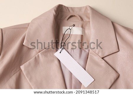 Blank white tag on beige leather jacket, top view. Space for text